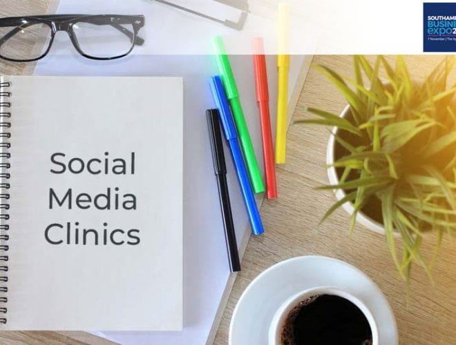 Pens and coffee on a wooden table along with a notebook that says 'social media clinic'