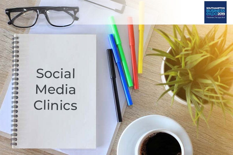 Pens and coffee on a wooden table along with a notebook that says 'social media clinic'