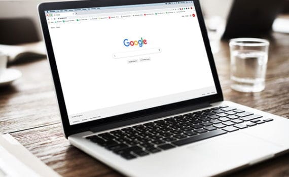 laptop on a wooden table with the Google search page on the screen