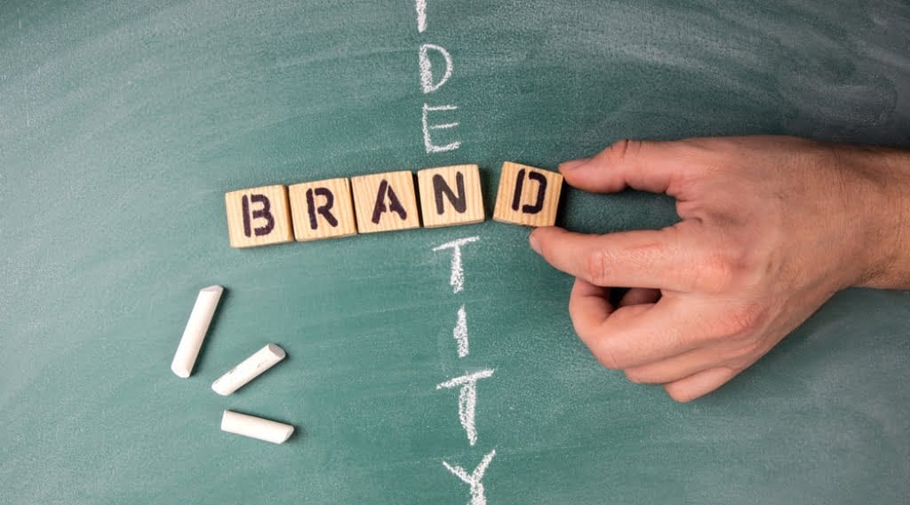 A stylised image depicting brand identity; hands moving wooden blocks spelling the word 'brand' intersected by the word identity written in chalk