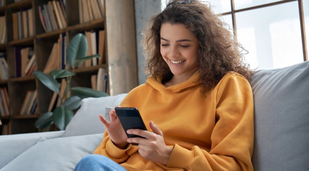 A young woman is entertained by a smartphone while sitting on a sofa