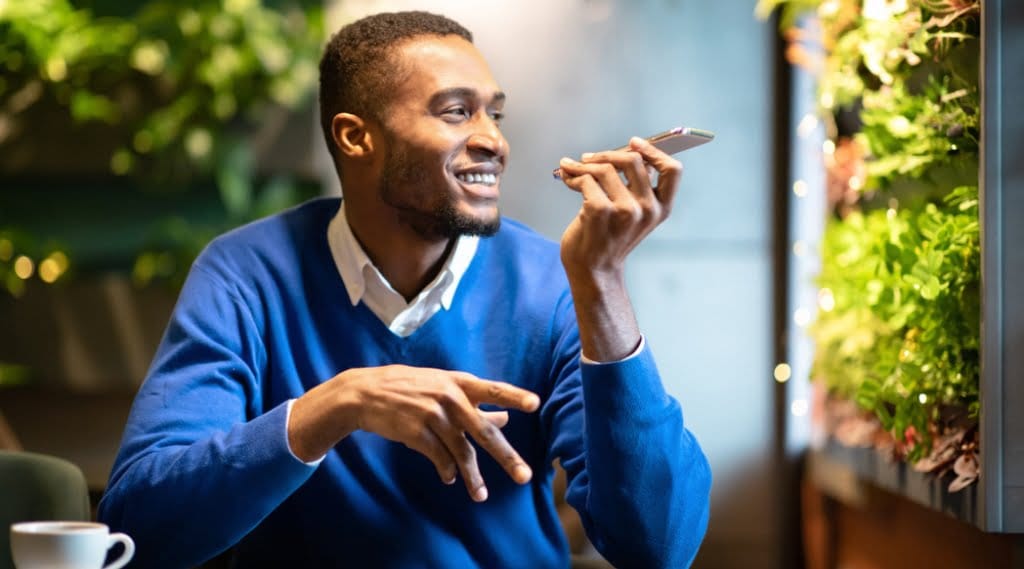A man in a jumper sits at a table using voice search on a smartphone
