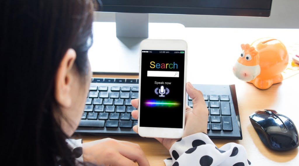 Someone uses voice search on their smartphone while sitting at their desk