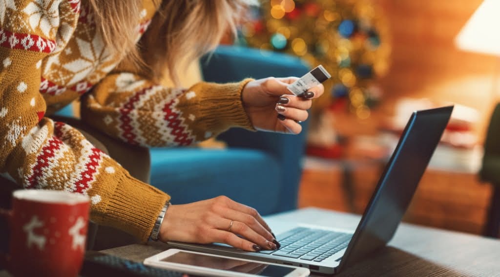 A woman in a festive jumper makes a purchase on a laptop
