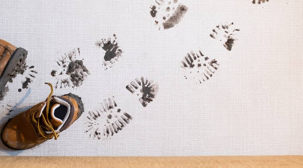 Muddy boot prints tracked across a clean white floor, with a pair of worn work boots, illustrating the concept of a visible digital footprint.