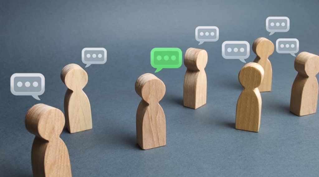 Wooden figures with speech bubbles, one highlighted in green, representing customer retention through word of mouth.