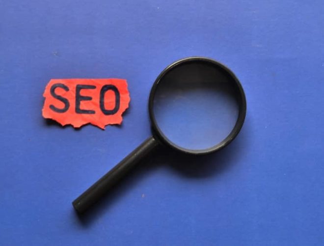 Magnifying glass beside red paper reading “SEO,” symbolising SEO agency and SEO packages.