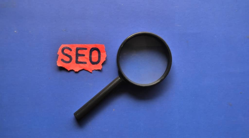 Magnifying glass beside red paper reading “SEO,” symbolising SEO agency and SEO packages.