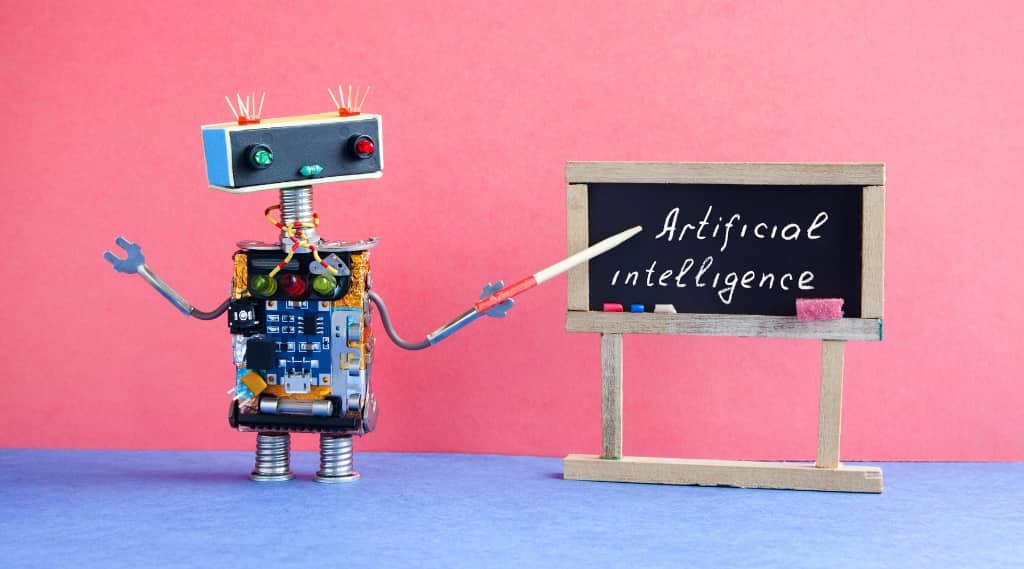 Small robot pointing to chalkboard reading “Artificial Intelligence,” representing teaching AI for better search results.