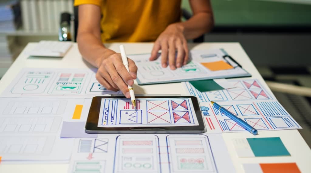 UX designer sketching and planning layouts on tablet and paper wireframes