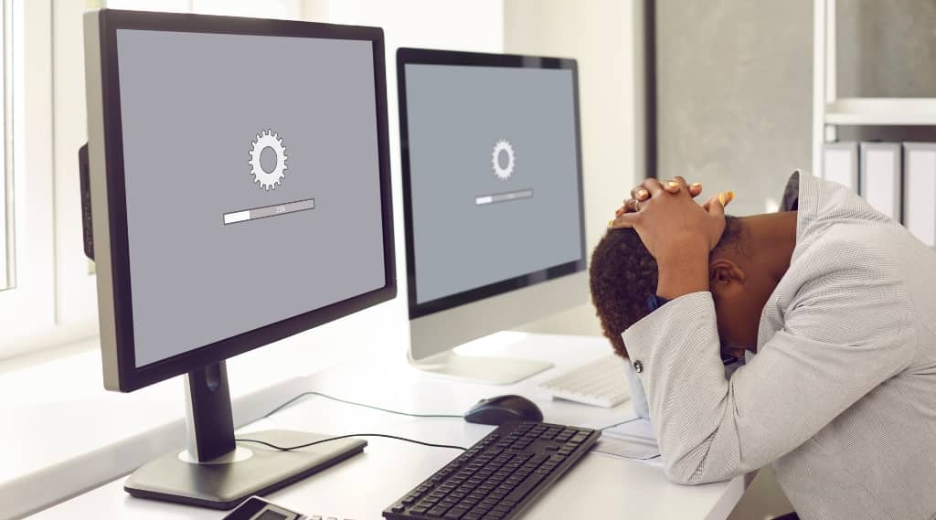 Frustrated worker with head in hands in front of slow-loading computer screens, representing slow site speed and bad conversion rates.