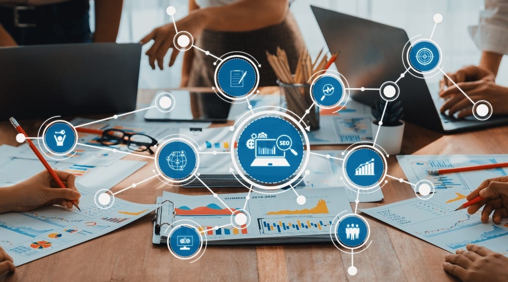 Ai search optimisation SEO strategy, a team working around a table with laptops and charts overlaid with connected digital SEO and analytics icons