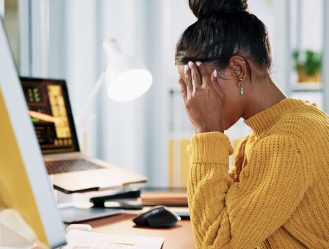 bad website design reaction, a frustrated woman in a yellow jumper holding her head in her hands at a desk with her computer