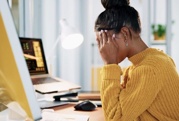 bad website design reaction, a frustrated woman in a yellow jumper holding her head in her hands at a desk with her computer