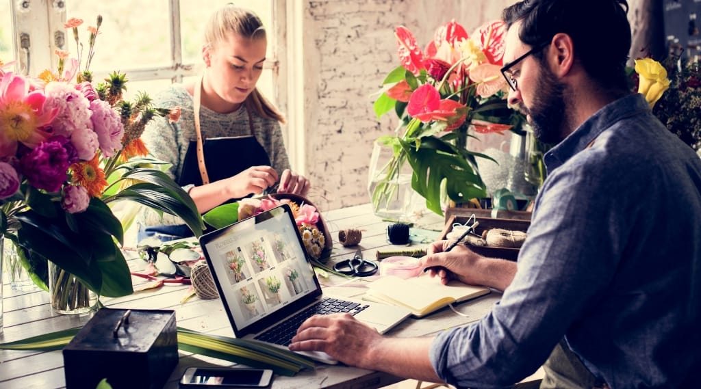 small business web design florist, a florist workshop where two people work with flowers beside an open laptop showing an online shop
