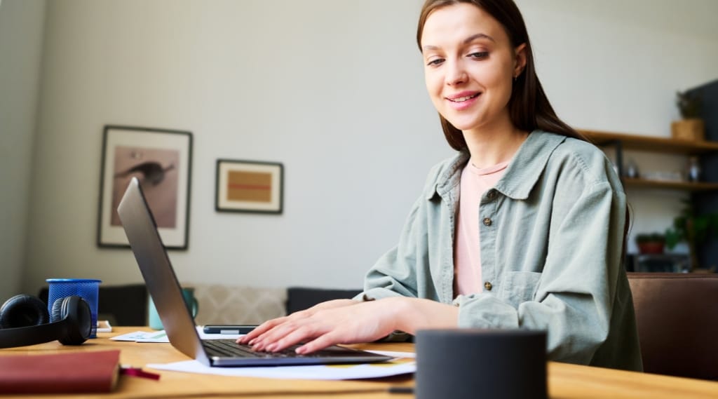 voice activate AI search optimisation, a woman smiling while working on a laptop with a smart speaker on her desk