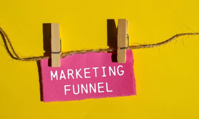 What is the marketing funnel: Marketing funnel sign clipped to a string against a yellow background, illustrating what a marketing funnel is and how it works.