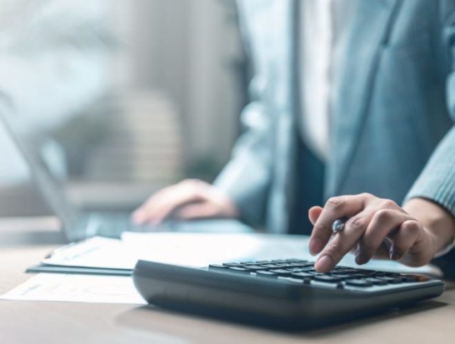 Should you cut your marketing spend: business professional using a calculator at a desk reviewing documents.