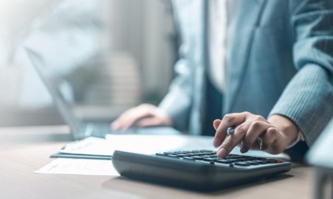 Should you cut your marketing spend: business professional using a calculator at a desk reviewing documents.