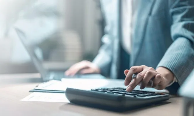 Should you cut your marketing spend: business professional using a calculator at a desk reviewing documents.