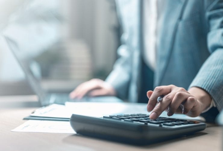 Should you cut your marketing spend: business professional using a calculator at a desk reviewing documents.