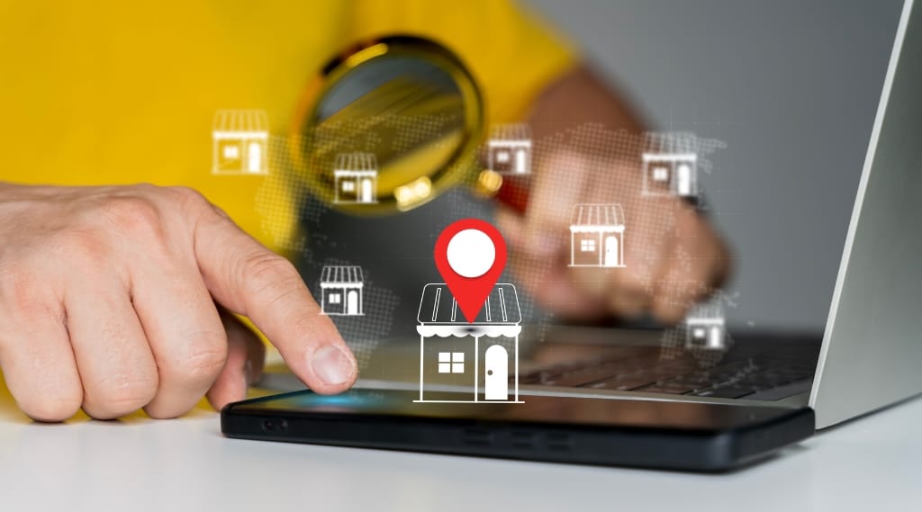 Person pointing at smartphone and laptop with map pin and store icons, illustrating SEO services in Hampshire and local search visibility.