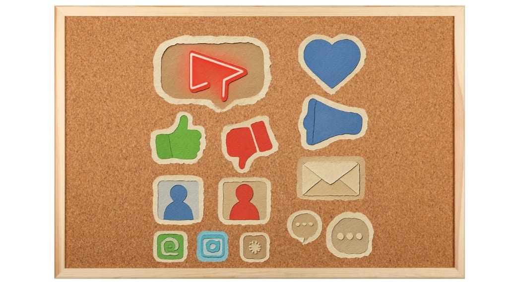 Social media feedback "Cork noticeboard displaying various paper-cut social media icons including a play button, heart, thumbs up, thumbs down, megaphone, profile icons, email envelope, and message bubbles"