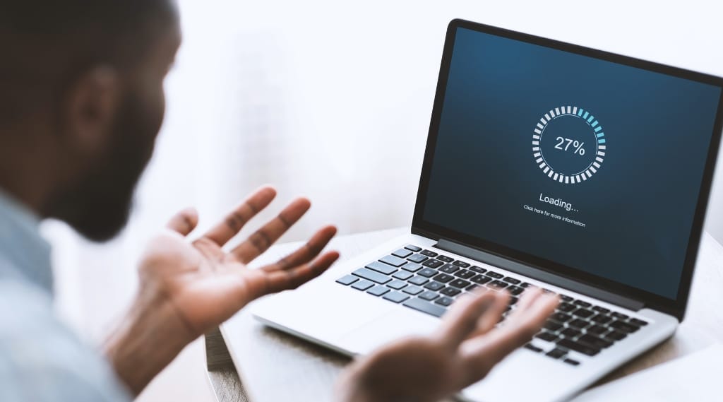 Website optimisation "Frustrated man gesturing with his hands at a laptop screen displaying a slow-loading progress bar stuck at 27%"