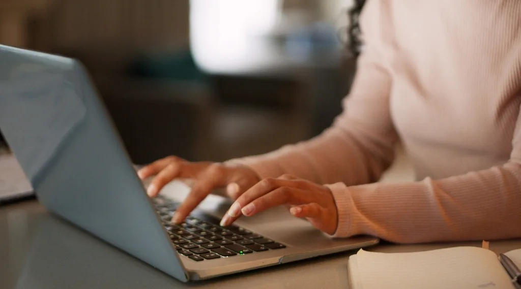 Content optimisation "Close-up of a person's hands typing on a laptop keyboard, with an open notebook beside them"