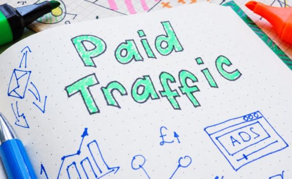 what makes a good landing page for paid ads: A handwritten notebook page reading "Paid Traffic" in green bubble lettering, surrounded by doodled charts, arrows, a pound sign and an ad browser icon, with coloured marker pens resting on the page.