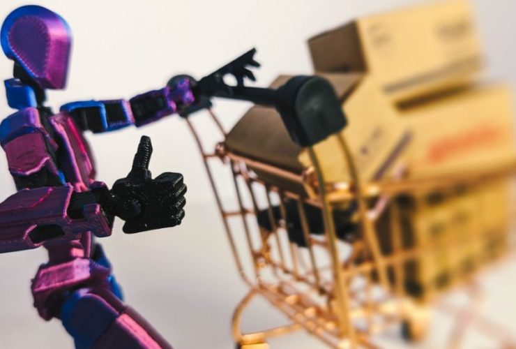 How AI Shopping Agents Choose Products for Black Friday: A purple and blue jointed robot figure gives a thumbs up while pushing a miniature copper shopping trolley loaded with cardboard parcels.