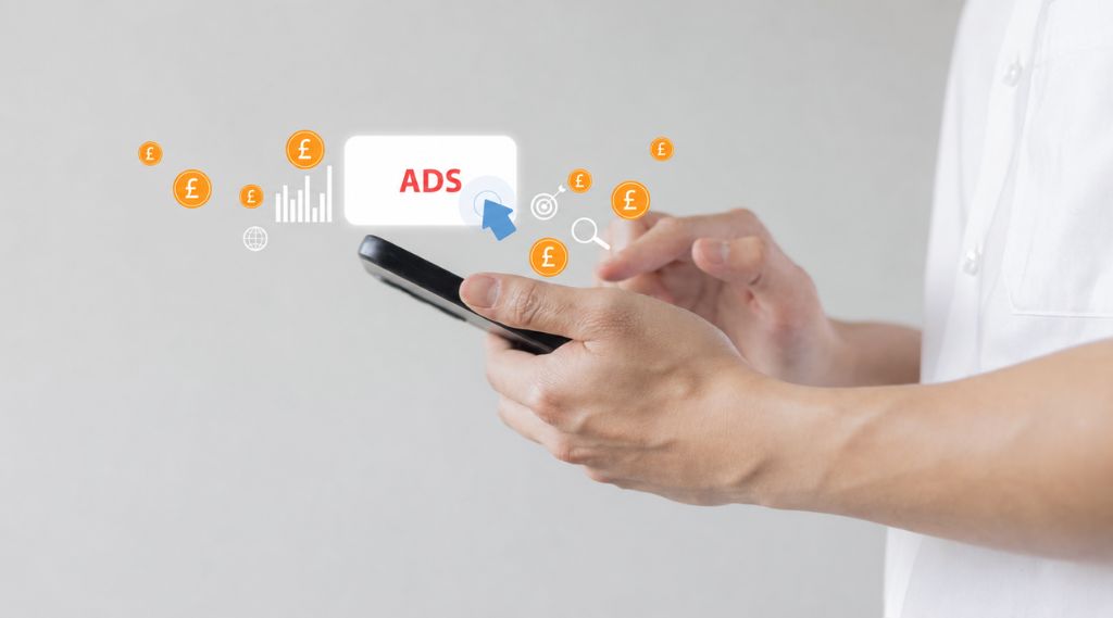 award-winning SEO agency Hampshire: A person in a white shirt taps a smartphone, with floating icons rising from it: a white “Ads” button being clicked, orange pound coins, a bar chart, a target and a magnifying glass, against a light grey background.