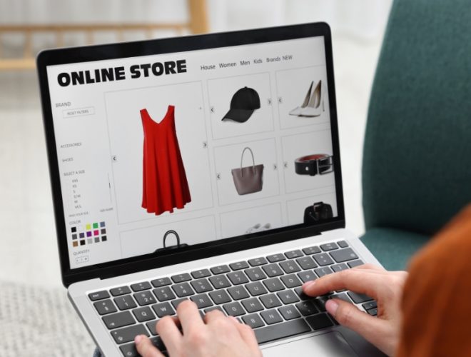 does my business need a website in 2026: A person typing on a laptop while browsing an online store website showing a red dress, black cap, white heels, handbag and belt, illustrating how customers shop with businesses online in 2026.