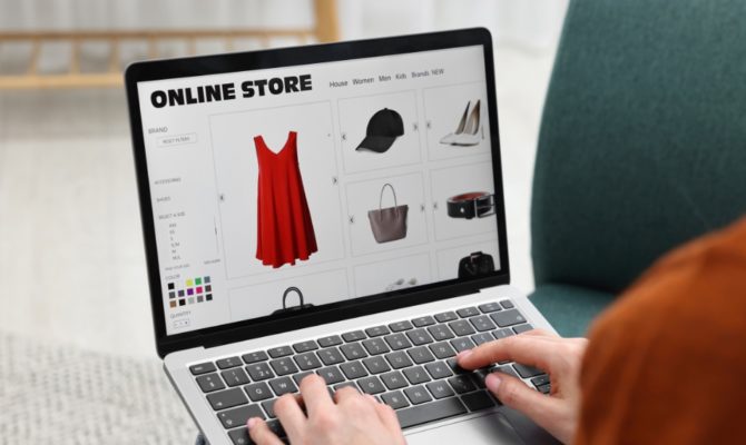 does my business need a website in 2026: A person typing on a laptop while browsing an online store website showing a red dress, black cap, white heels, handbag and belt, illustrating how customers shop with businesses online in 2026.