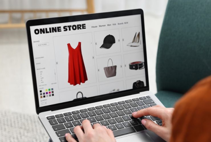 does my business need a website in 2026: A person typing on a laptop while browsing an online store website showing a red dress, black cap, white heels, handbag and belt, illustrating how customers shop with businesses online in 2026.
