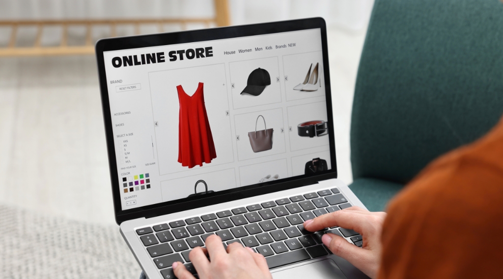 does my business need a website in 2026: A person typing on a laptop while browsing an online store website showing a red dress, black cap, white heels, handbag and belt, illustrating how customers shop with businesses online in 2026.