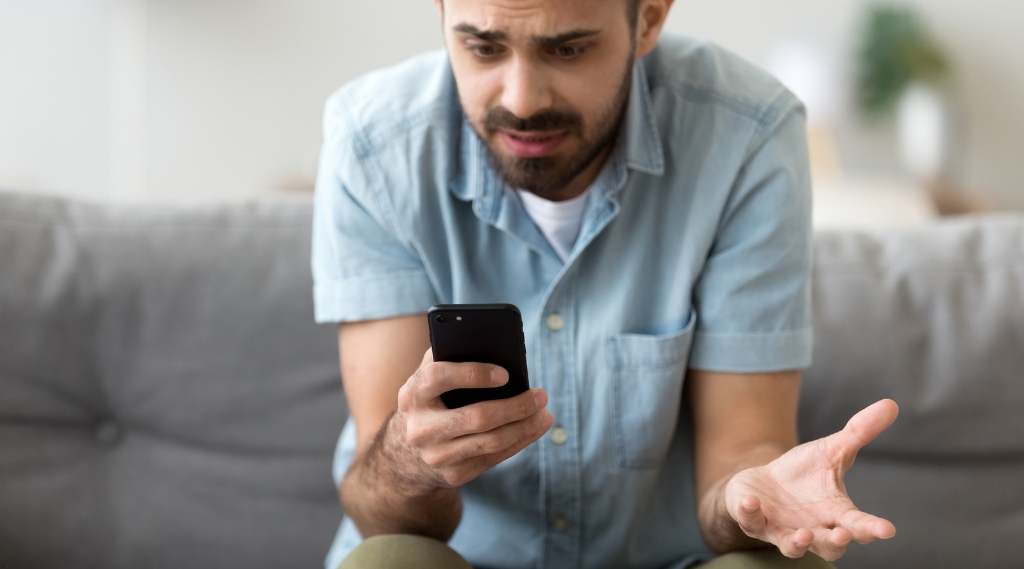 how do I stop wasting money on Google Ads: A frustrated man on a sofa staring at his smartphone with his hand held out in confusion, reacting to Google Ad directing him to the wrong landing page.