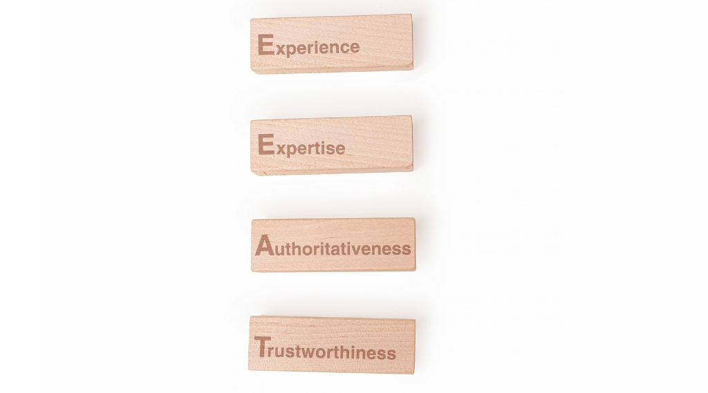 what SEO mistakes hurt your website ranking: Four wooden blocks on a white background engraved with Experience, Expertise, Authoritativeness and Trustworthiness, the Google E-E-A-T signals that affect website ranking when they're missing.