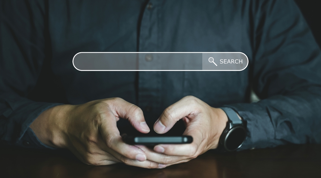 why is my Google Ads budget being wasted: A man in a dark shirt holding a smartphone beneath a blank search bar overlay, representing the search clicks that use up a Google Ads budget without converting.